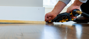 An air nailer being used to install baseboard.