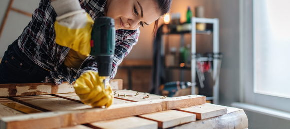A woman using a power drill to drive a screw into a piece of lumber.